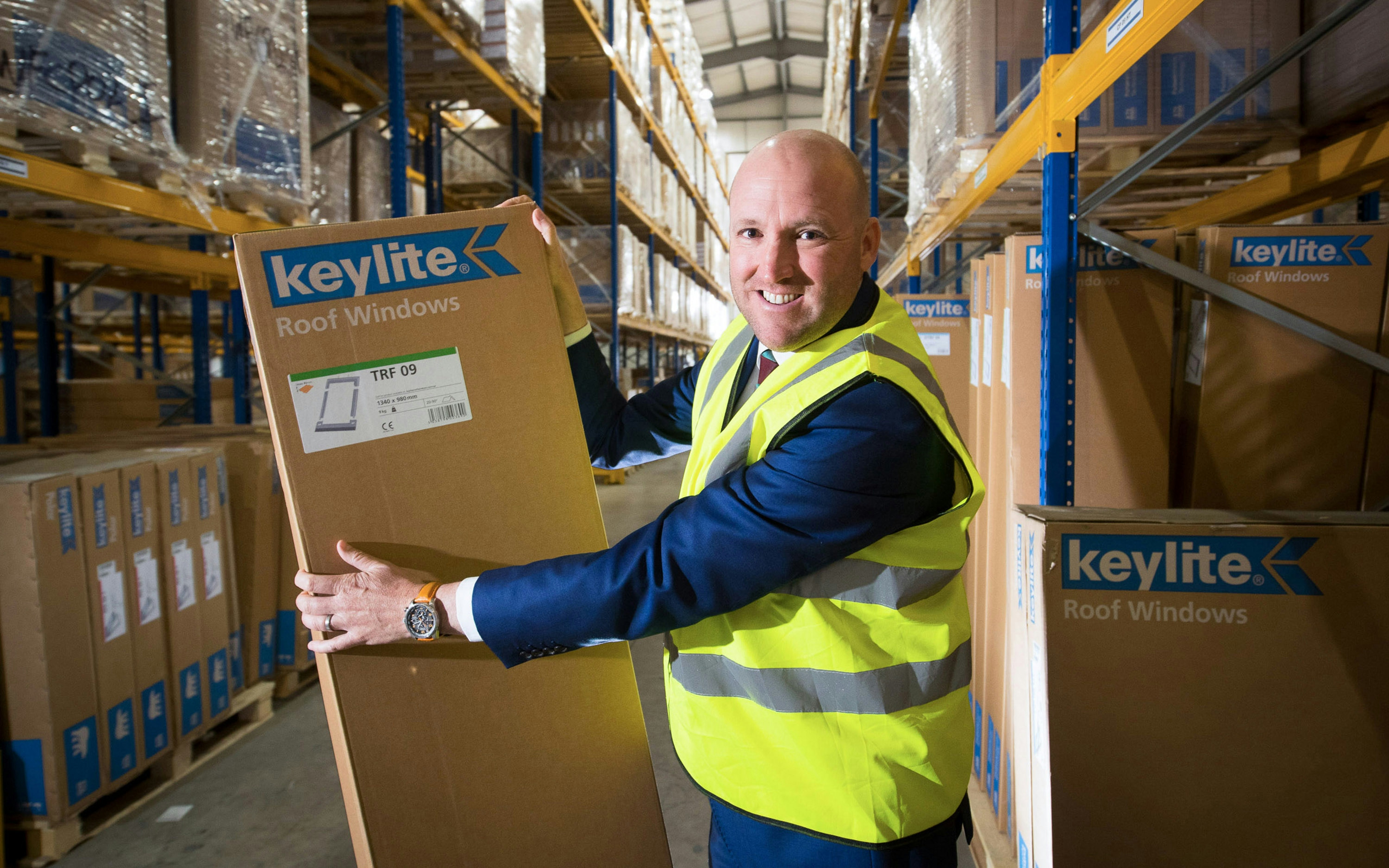A man in a hi-vis holding a box in a warehouse